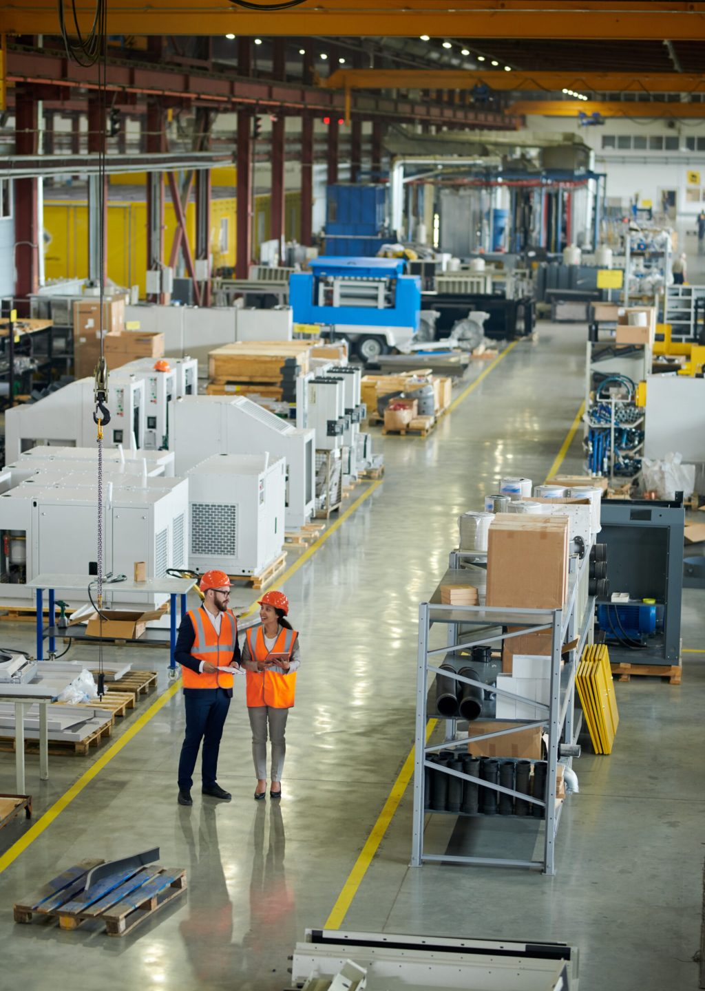 High angle full length portrait of bearded businessman wearing hardhat inspecting production workshop accompanied by smiling young woman, copy space